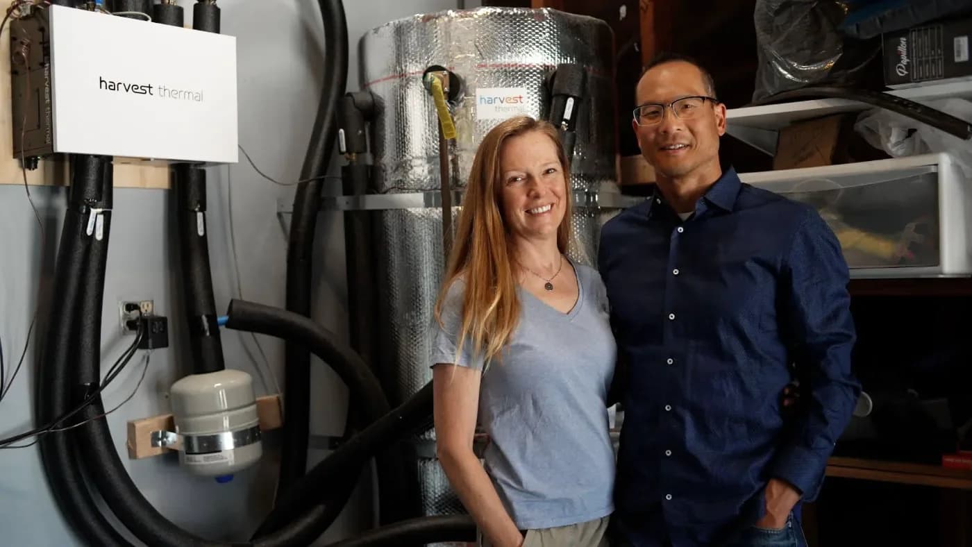Homeowners beside a Harvest controller and thermal storage tank, shown in Harvest manufacturer photography
