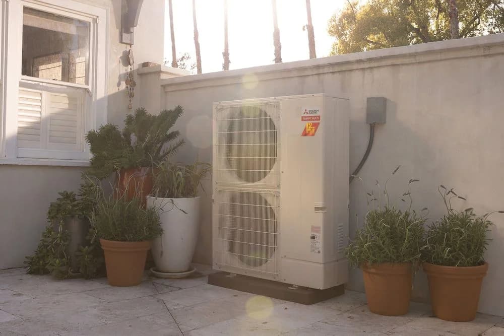 Mitsubishi Electric outdoor heat pump beside a home and planted patio